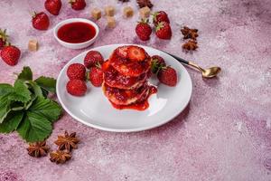 Cottage cheese pancakes with sliced strawberries and strawberry jam on a plate on a concrete background photo