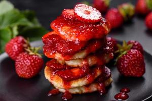 Cottage cheese pancakes with sliced strawberries and strawberry jam on a plate on a concrete background photo