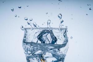 Ice cube fell into the glass of water. Water splashed from the clear glass. Fresh concept photo