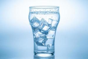 el cubo de hielo cayó en el vaso de agua. agua salpicada del cristal transparente. concepto fresco foto