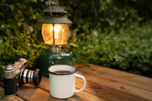 Selective focus white enamel coffee mug and coffee set in the garden with ancient lanterns in a camping atmosphere. soft focus. photo