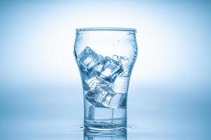 el cubo de hielo cayó en el vaso de agua. agua salpicada del cristal transparente. concepto fresco foto