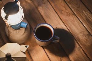 enfoque selectivo taza de café de esmalte blanco y juego de café en el jardín con farolillos antiguos en un ambiente de camping. enfoque suave. foto