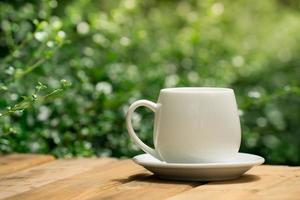 taza de café de cerámica blanca en el suelo de madera, fondo de bokeh de árbol verde. enfoque suave efecto de enfoque superficial. foto