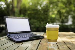 coffee cup paper with a Computer laptop in green nature background. Work remotely or from home. soft focus.shallow focus effect. photo