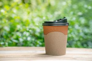 paper coffee cup on the wooden floor, green tree bokeh background. soft focus.shallow focus effect. photo