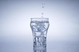 cubo de hielo cayó en el vaso de agua. agua salpicada del cristal transparente. concepto fresco foto