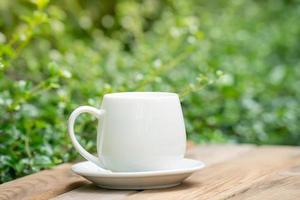 white ceramic coffee mug On the wooden floor, green tree bokeh background. soft focus.shallow focus effect. photo