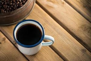 taza de café de esmalte blanco y granos de café oscuros en el viejo piso de madera. enfoque suave efecto de enfoque superficial. foto