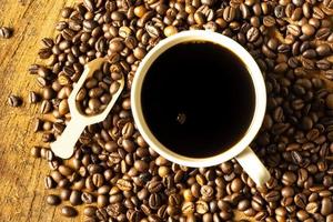 café negro en la taza, granos de café oscuros en el viejo piso de madera, cerca de semillas de café. foto