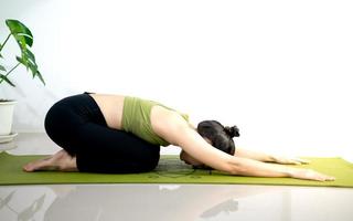 mujer haciendo yoga en la alfombra de yoga verde para meditar y hacer ejercicio en el hogar. foto