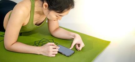 Women playing mobile and sitting on the green yoga mat while rest for a doing practice in the home. photo