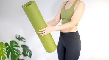 mano femenina sosteniendo una alfombra de yoga verde para preparar el ejercicio en la alfombra. foto