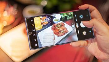 mujer sosteniendo un teléfono inteligente y tomando una foto con la comida de vietnam para mostrarla en sus redes sociales.