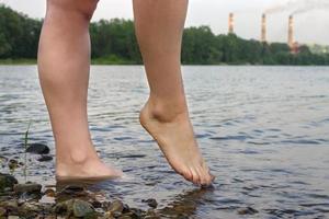 chica de pies en el río en el fondo de las tuberías de fábrica liberando humo. el problema de la contaminacion ambiental foto