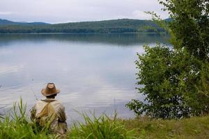 el pescador se sienta junto al lago. vista trasera. foto