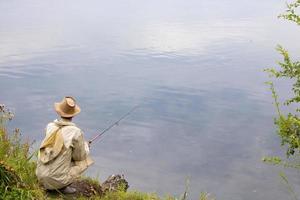 el pescador se sienta junto al lago. vista trasera. foto