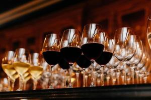 Many glasses filled with white and red wine on table. Dark colours. Wine collection. Horizontal shot. Beverage in wine glasses photo