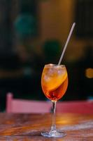 Aperol spiritz cocktail contains alcohol and juice, cold ice and orange, stands in wine glass on wooden table, served in restaurant for visitors photo