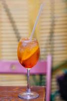 Aperitif cocktail consisting of prosecco, Aperol and soda water, stands in wine glass on wooden table in bar. Aperol spiritz cocktail with several cubes of ice and slice of orange. photo