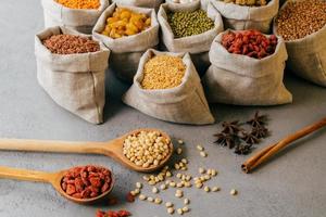Horizontal view of small sacks with various colorful dry ingredients, two wooden spoons and star anise near. Healthy dieting concept photo