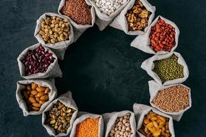 Top view of colorful nutritious cereals and dried fruit in small sacks standing in circle, isolated over dark background. Food concept photo