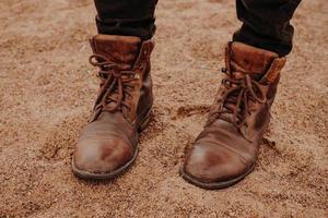 Image of unrecognizable man stands on sandy ground in brown leather old shaggy shoes with laces. Mens footwear. Outdoor shot photo