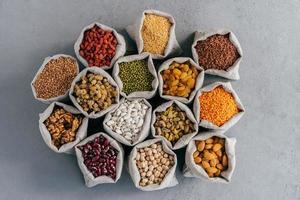 Raw healthy grain food and legume. Hessian bags of cereals and dried fruit. Packing groats at market against grey background photo