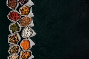 Photo of healthy food ingredients in little sacks, isolated over black background with empty space for your promotion. Bags of cereals and beans, fruit in one row