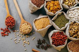 Husbandry and nutrtion concept. Top view of various beans and colorful dried fruit packed in little burlap sacks. Wooden spoon with ingredients photo