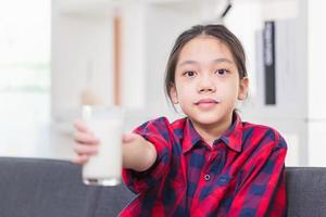 Happy child girl drinks milk, Portrait of Asian little cute kid holding a cup of milk in kitchen photo