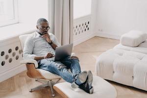 Confident professional at work in front of laptop. Relaxed african businessman in cosy chair. photo