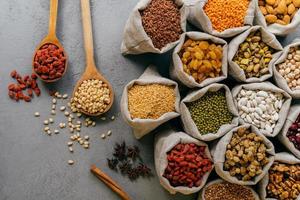 Organic food concept. Nutritious ingredients in burlap sacks, star anise, spilled cerelas from spoons on grey background photo