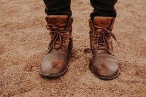 Shot of male stands sandy ground, wears old shaggy shoes, shows footwear. Horizontal view. Man has walk outside. Outdoor photo