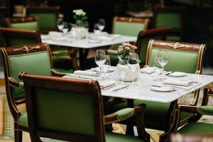 Table served with luxury glasses, cutlery, flowers, green chairs around in cozy restaurant. Nobody in shot. Decorated table for festive event photo