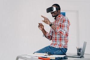 African american student in vr glasses at home. Young businessman has remote virtual study. photo