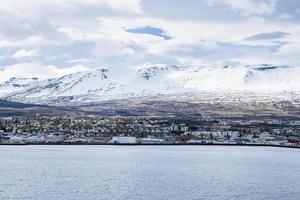 Scenic view of cityscape at seashore with snowcapped mountains in background photo