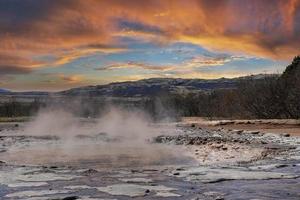 Smoke emitting from geothermal field at Smidur Geyser valley against cloudy sky photo