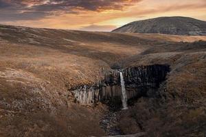 vista de la cascada svartifoss en medio de columnas de basalto y acantilados durante la puesta de sol foto