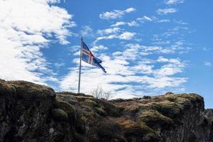 Icelandic flag waving on rocky cliff against blue cloudy sky photo