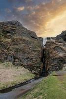 Idyllic view of Gljufrafoss hidden amidst mountain against cloudy sky at sunset photo