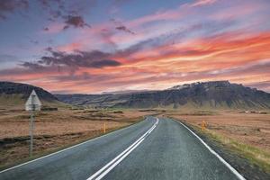 carretera vacía que conduce a la cordillera contra el cielo nublado durante la puesta de sol foto