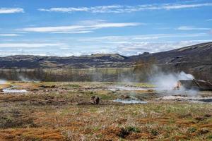 View of geothermal smoking field at Smidur Geyser valley against blue sky photo