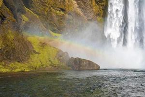View of beautiful rainbow over rock formations and Skoga river against Skogafoss