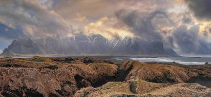 Grass on black beach against Stokksnes cape and Vestrahorn Mountain at sunset photo