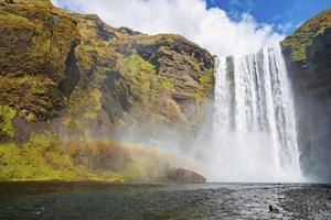 Low angle view of beautiful Skogafoss waterfall falling from cliffs against sky photo