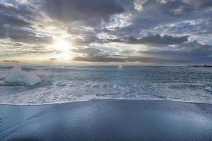 Scenic view of waves rushing at black sand shore of Diamond beach against sky photo