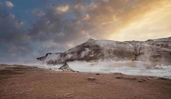 Steam emitting from crater in geothermal area of Hverir against sky during sunset photo