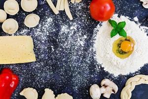 Raw pizza dough with ingredients and spices on dark background. Top view photo