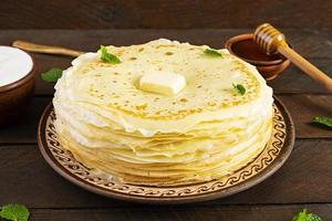 Delicious crepes with honey and sour cream on wooden background photo
